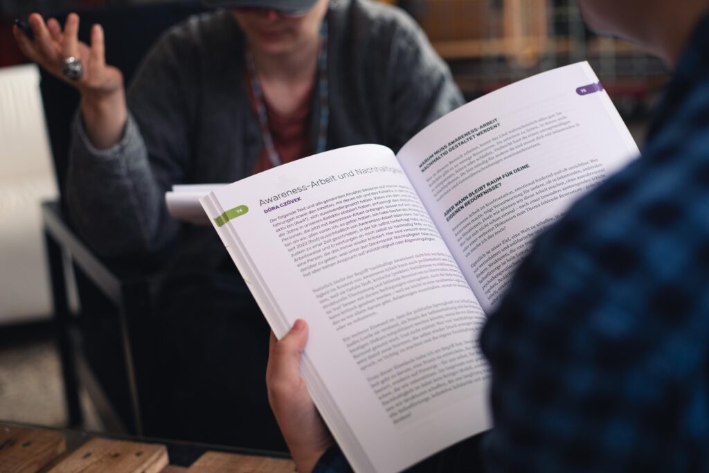 Awareness Broschüre Innenseite gehalten von einer Person mit einer anderen Person im Hintergrund im Gespräch