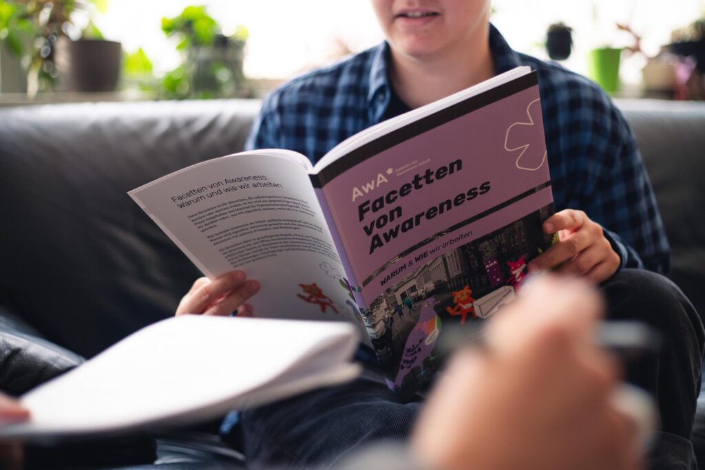 Awareness Broschüre Cover gehalten von einer Person mit einer anderen Person im Vordergrund im Gespräch